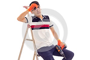 Young man holding electric screwdriver and sitting on ledder