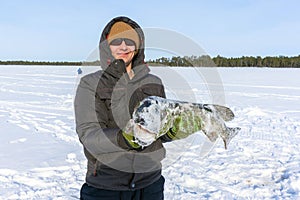 Young man holding fish catch a big pike ice fishing