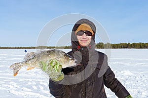 Young man holding fish catch a big pike ice fishing