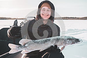 Young man holding fish catch a big pike ice fishing