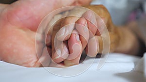 Young man holding and gentle touching hand of sick mature woman in hospital. Grandson comforting wrinkled arm of his old