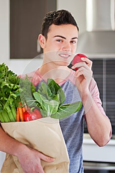 Young man holding groceries eating an apple