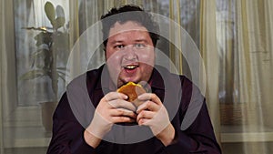 Young man holding a hamburger. Fat guy eats fast food. Burger is not helpful food. Very hungry guy.