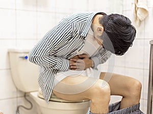 Young man holding his abdomen feels sick and constipation in the toilet