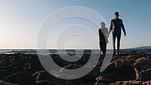 Young man holding his girlfriend`s hand and walking on beach at sunset.  Man and woman enjoying sea on beach. Silhouette of loving