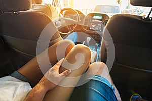 Young man holding his hand on the leg tanned young girl sitting in the back seat of the car