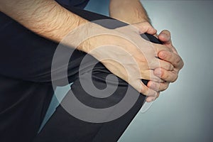 young man is holding his hands over his sick knee on a blue background. patella fracture, athlete in a tracksuit with a pain in th