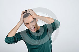 Young man holding his head frowning with worry screaming.