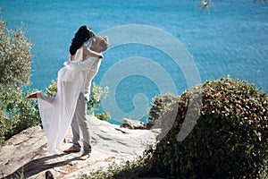 Young man holding his sexy brunette woman in arms, they kissing. They are standing in a beautiful seascape near the sea.
