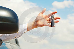 Young man holding keys remote from his car in hands over sky background