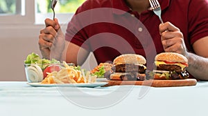 Young Man holding knife and fork are ready to eating a hamburger, French fries, and Spaghetti for Lunch. Concept of binge eating