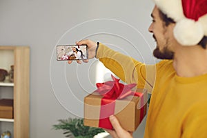 Young man holding mobile, making video call and showing his girlfriend her Christmas present