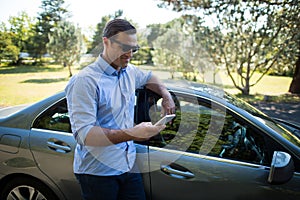 Young man holding mobile phone by car