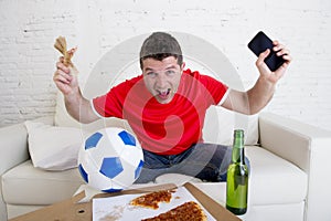 Young man holding mobile phone and money in his hands watching fottball game on television internet gambling concept