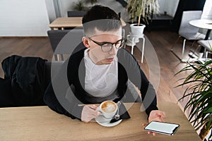 Young man holding mobile phone. He is sitting in restaurant or cafe. He is trying to watch a video or movie. Place for