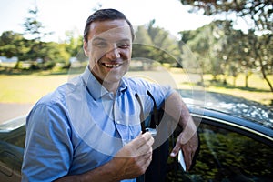 Young man holding mobile phone and sunglasses by car