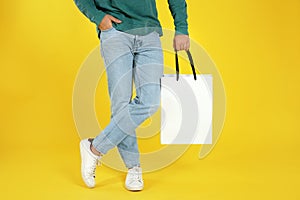 Young man holding paper bag on color background
