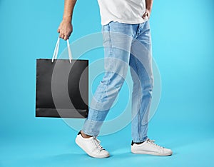 Young man holding paper bag on color background, closeup.