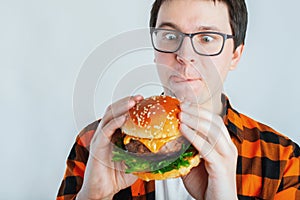 Young man holding a piece of hamburger. Student eats fast food. Burger is not helpful food. Very hungry guy looks at the burger an