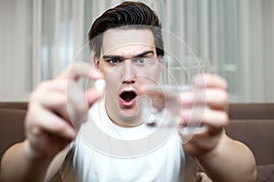 Young man holding pill and glass of water suffering headache after partying handover