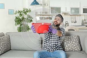 Young man holding plastic basin under water leakage from ceiling at home.