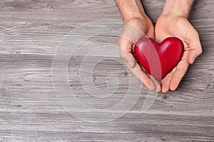 Young man holding red heart on grey wooden background, top view. Donation concept