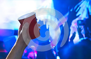 Young man holding red party cup in nightclub dance floor. Alcohol container in hand in disco.