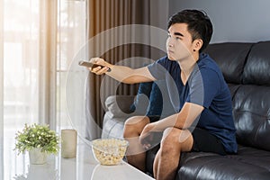 Young man holding remote control and watching TV while sitting o