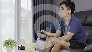 Young man holding remote control and watching TV while sitting on sofa