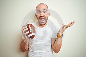 Young man holding rugby american football ball over isolated background very happy and excited, winner expression celebrating