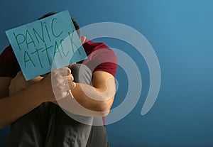 Young man holding sheet of paper with words PANIC ATTACK on color background