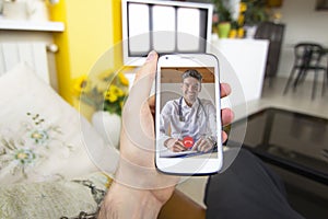 Young man holding smartphone making video call with doctor at home