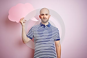 Young man holding speech bubble with blank space for message over pink isolated background with a confident expression on smart