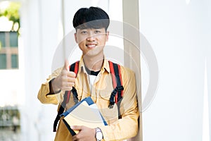 A young man is holding a stack of books and giving a thumbs up