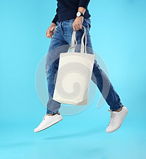 Young man holding textile bag on color background, closeup.