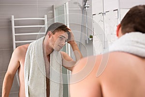 Young man holding towel on his shoulders while viewing a mirror