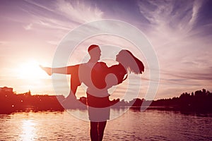 Young man holding woman on summer river bank. Couple having fun at sunset. Guys chilling