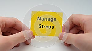 A young man holding a yellow paper note with the words Manage Stress on it in his hands.