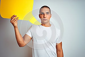 Young man holding yellow speech bubble over white isolated background with a confident expression on smart face thinking serious