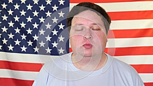 Young man holds back laughter on the background of an USA flag