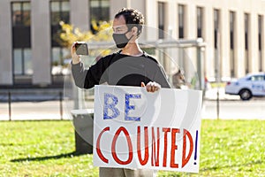 A young man holds a banner that says be Counted referring to vote counting
