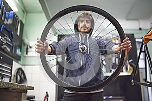 Young man holds a bicycle wheel rim in his bike repair shop. Real people at work