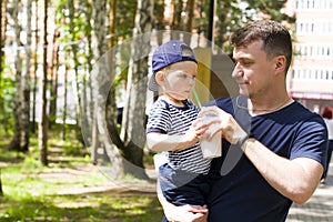 a young man holds a child in his arms, gives the baby a milkshake to drink. Father and son in the Park on a family vacation drink.