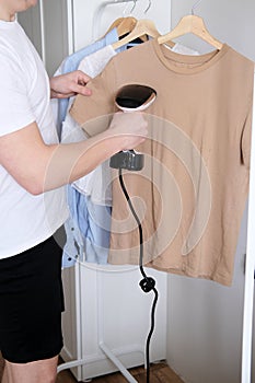 A young man holds the garment steamer in his hand and smoothes the t-shirt after washing and drying