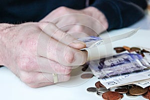 Young man holds a GBP twenty pounds money note and coins are liyng on a table around