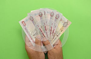 Young man holds in his hands dirhams on green background. AED.