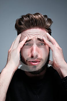 A young man holds his head and shows different human emotions: hatred, fear, despair, horror, malaise, headache, clairvoyance.