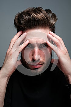 A young man holds his head and shows different human emotions: hatred, fear, despair, horror, malaise, headache, clairvoyance.