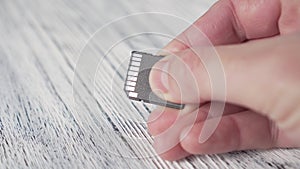 A young man holds a MICRO SD MEMORY CARD in his hand over a white textured wooden table