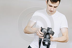 A young man holds a photo camera in his hand and looks at the photo on the photo camera. Isolated gray background photo